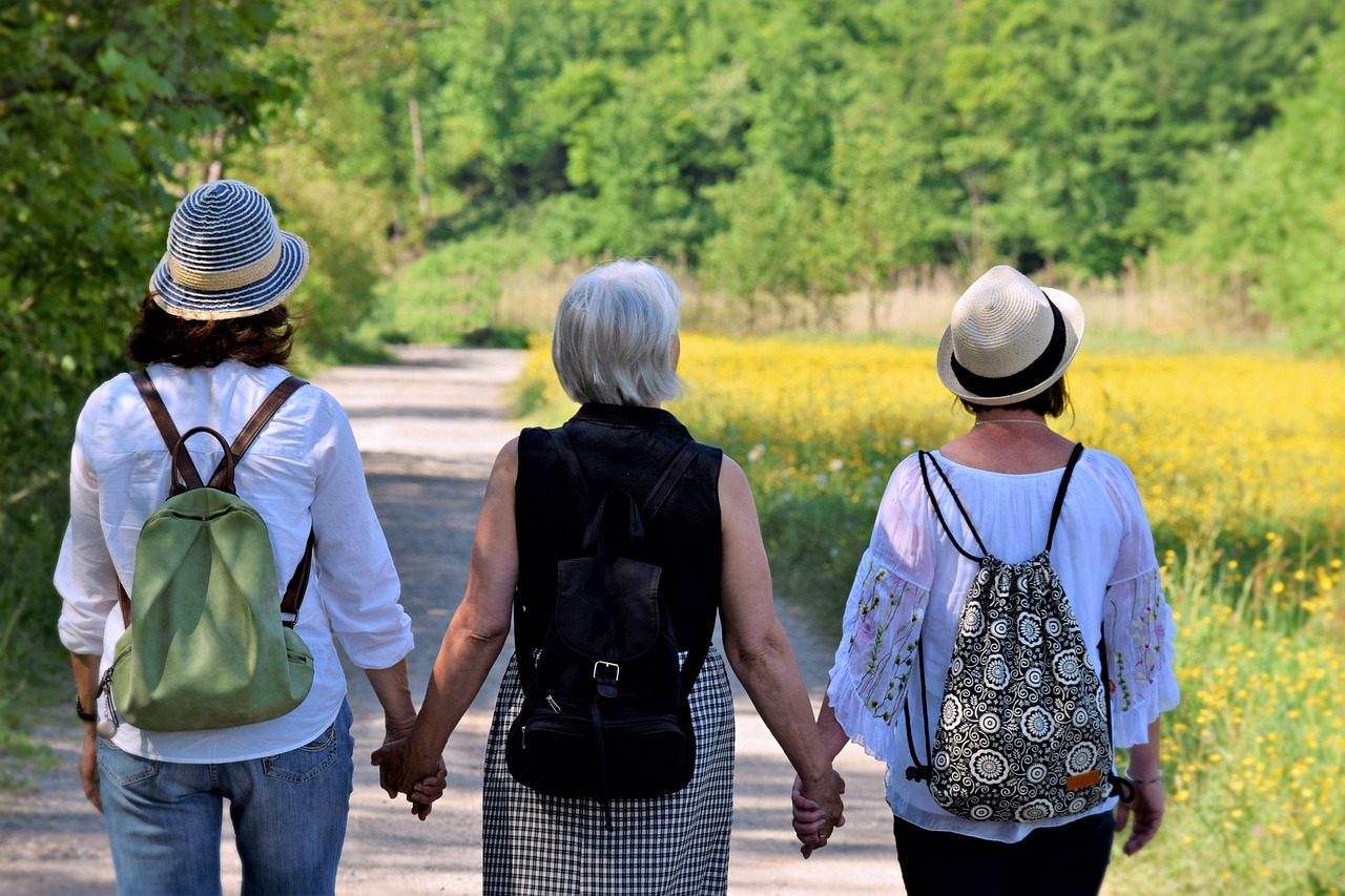 Three women, seen from behind, walking on a nature walk, holding hands