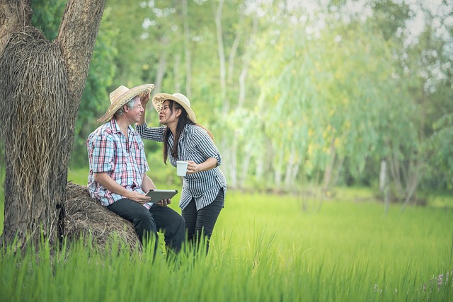 Man sitting on a tree trunk, white hair, hat, flirting with a woman with black hair, also wearing a hat.