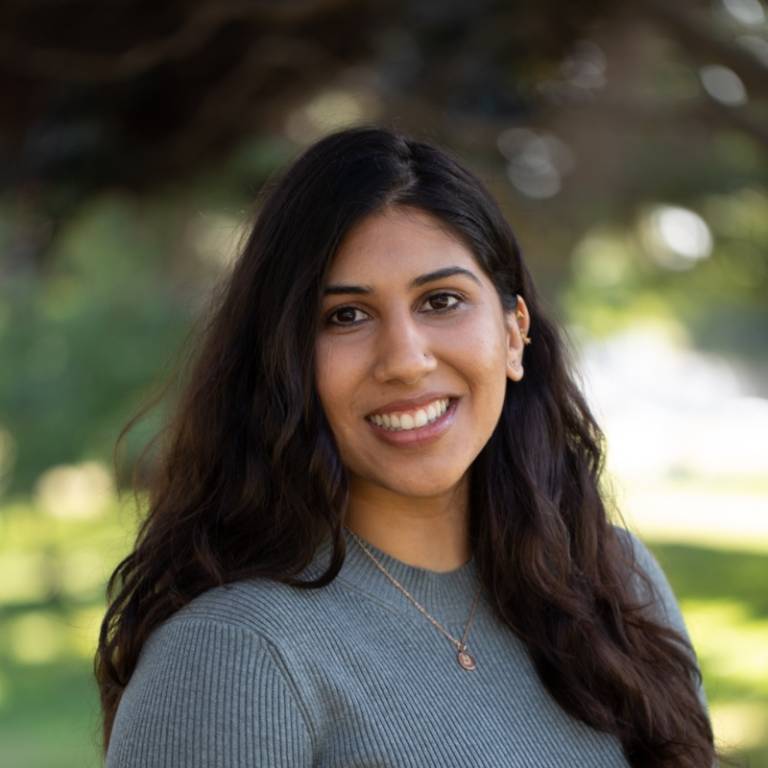 Daniya Ahmed, LMFT smiling, looking directly into camera, long brown hair over her left shoulder, blurred greenery in the background