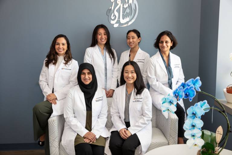 Physicians and PA of ECWMG sitting on a couch, all wearing white coats, looking at the camera, smiling